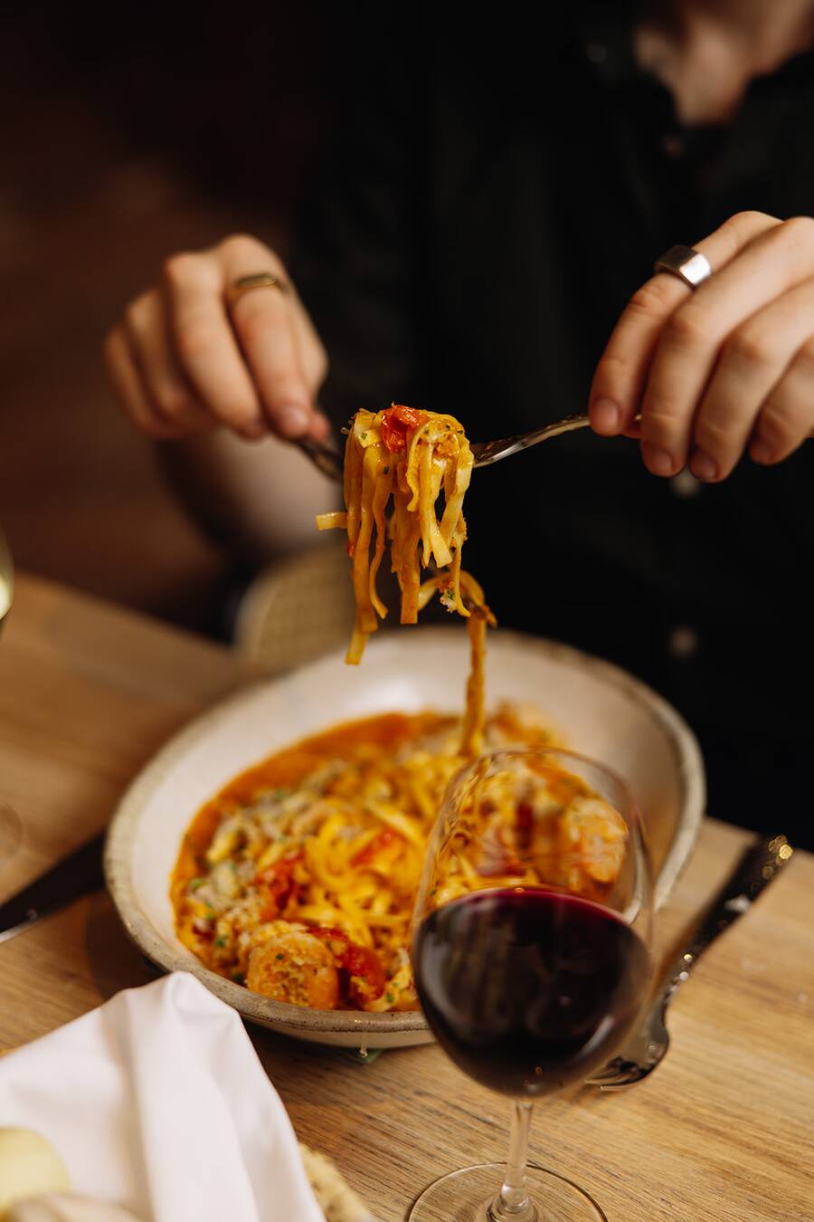 Fresh pasta being lifted from a bowl beside a glass of red wine